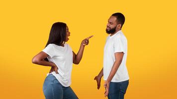 Angry Black Woman Blaming Husbang For Problems In Marriage, Scolding And Pointing Finger At Him, Upset Man Listening Complaints From His Wife. Couple Suffering Relationship Crisis, Yellow Studio photo