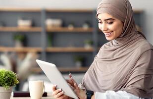 Technology. Millennial Muslim Woman Spending Time With Digital Tablet Sitting At Desk At Home Office, Reading News, Browsing Internet, Watching Videos, Checking Social Networks, Free Copy Space photo
