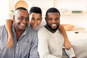 Happy african boy hugging his father and grandpa while posing to camera at home, bonding together, free space photo