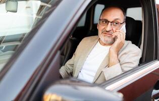 un hombre en un ligero chaqueta de sport es sentado en el conductor asiento de un estacionado auto, comprometido en un teléfono conversación. él aparece considerado, mirando fuera de el ventana en un urbano ajuste. foto