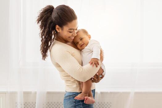 amoroso africano americano madre participación bebé acurrucarse niñito en brazos disfrutando maternidad y niño cuidado en pie adentro. contento maternidad momentos, mamá y infantil enlace concepto foto