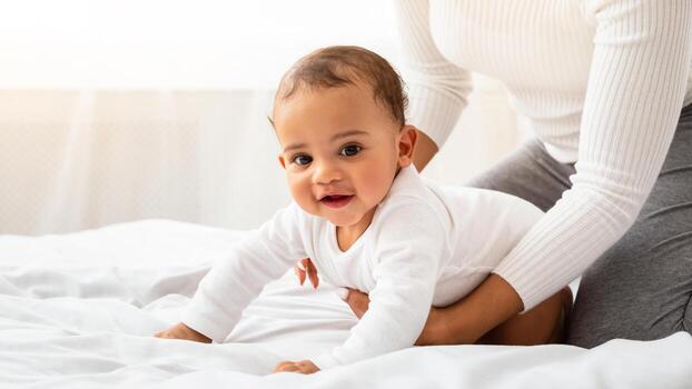 irreconocible negro mamá Ayudar bebé hijo gatear en cama jugando con pequeño niñito durante maternidad salir sentado en dormitorio a hogar. recortado disparo. bebé chico mirando a cámara gateando interior foto