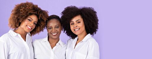 Friendship. Studio Portrait Of Three African American Ladies In White Shirts, Hugging Showing Their Unity, Expressing Good Vibes Smiling At Camera Together Over Purple Background photo