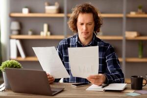 Serious Businessman Reading Business Reports And Financial Bills Looking Through Papers And Documents Sitting At Workplace In Modern Office. Selective Focus photo
