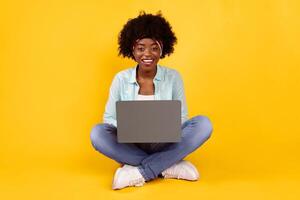 Happy African American Woman Using Laptop Smiling To Camera Sitting On Floor Posing Over Pink Background. Black Female Browsing Internet And Networking. E-Learning, Distant Work Online And Freelance photo