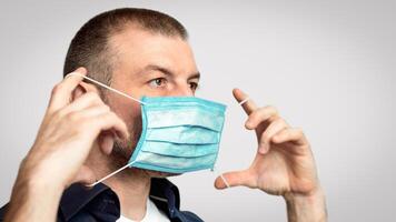 Mature Man Putting On Mask For Coronavirus Prevention Standing Over Gray Studio Background. Virus Protection Concept. Panorama photo