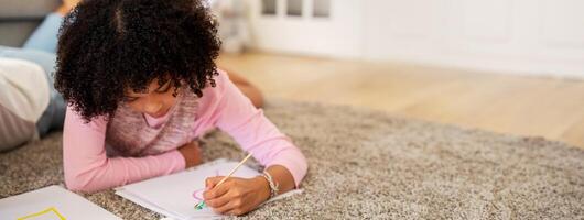 A black child enjoys her creative time by drawing colorful pictures on paper while comfortably lying on a soft carpet in her home, cherishing a quiet afternoon. photo