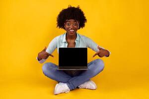 Happy Black Young Woman Showing Laptop Empty Screen Sitting With Computer Posing On Pink Background, Smiling To Camera. African Female Student Advertising Educational Website, E-Learning. Mockup photo