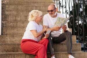 Happy couple sits on steps, engaged in conversation while studying a map. Their relaxed attire and joyful expressions reflect their enjoyment of exploring local sights together. photo