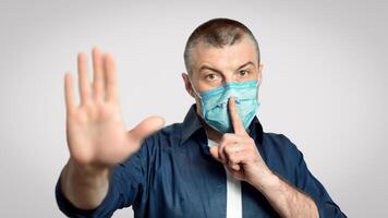 Don't Spread Panic. Man In Medical Mask Gesturing Hush Sign And Stop Gesture Over Gray Background During Pandemic. Selective Focus photo