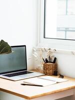 Close up view of wood table workspace with opened laptop and stationery near window in apartment photo