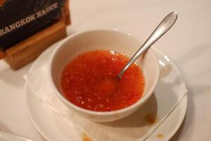 A bowl of red chili sauce sits on a white napkin photo