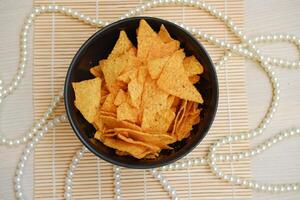 Nachos chips in a black bowl on a wooden table photo