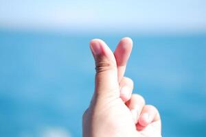A hand making a finger heart gesture with a blurred blue background. photo