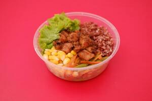 A plastic bowl filled with grilled chicken, red rice, fresh lettuce, corn, and mixed vegetables photo