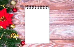 Festive Christmas composition with blank notepad for wish list and Christmas decoration on wooden background. Copy space. Flatlay. Top view. photo