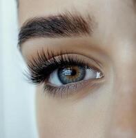 Detailed close-up of a blue eye with long, voluminous eyelashes and a well-shaped eyebrow. The photo captures the intricate iris and natural skin texture.
