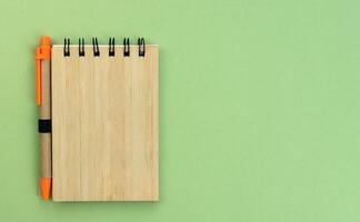 Flatlay composition with notebook and pen made of eco friendly materials on a green background. Top view. Copy space. photo