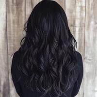 Back view of long, wavy black hair styled with soft curls, set against a rustic wooden background for a natural look. photo