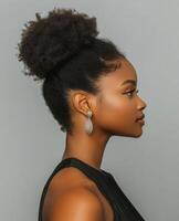 Side profile of a woman with a natural hair bun, wearing a black sleeveless top and statement earrings, set against a neutral background. photo