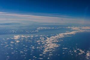 Aerial view from airplane window above green ground. View from the airplane window with beautiful clouds at sunrise. Earth and sky as seen through window of an airplane. photo