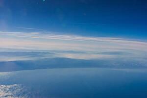 Aerial view from airplane window above green ground. View from the airplane window with beautiful clouds at sunrise. Earth and sky as seen through window of an airplane. photo