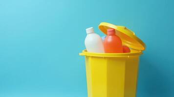 Bright yellow recycling bin with colorful plastic bottles against a blue background photo