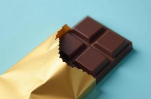 Unwrapped chocolate bar with gold wrapper on light blue background photo