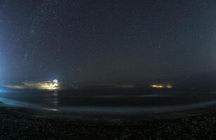 Thunderstorm cell over the sea at night with visible stars in the sky, creating a dramatic scene photo