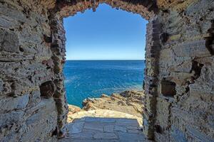View through an ancient stone archway leading to the rugged coastline and the open sea photo