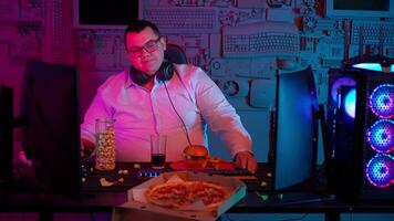 A man in glasses sitting at a desk with a pizza and a computer video