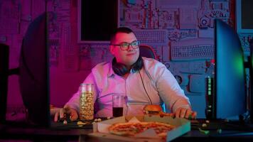 A man in glasses sitting at a desk with a pizza and a computer video