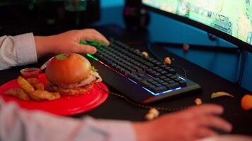 A person sitting at a desk with a burger and a computer video