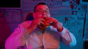 A man eating a hamburger in front of a computer screen video