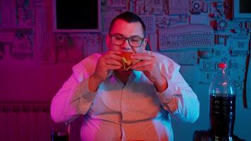 A man eating a burger in front of a computer video