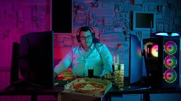 uma homem sentado às uma escrivaninha com uma pizza e uma computador video
