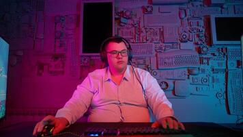 A man in glasses sits at a desk with a computer video