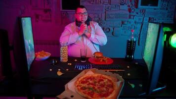 A man in glasses sitting at a table with a pizza and a computer video