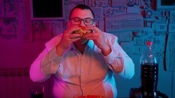 A man eating a burger in front of a computer video