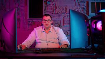 A man in glasses sitting at a computer with two monitors video