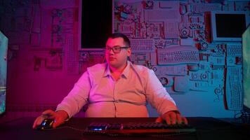 A man in glasses sitting at a desk with two computer monitors video