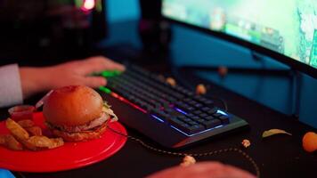 A person sitting at a desk with a burger and a keyboard video