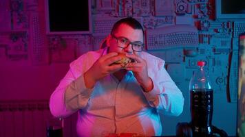 A man eating a burger in front of a computer video
