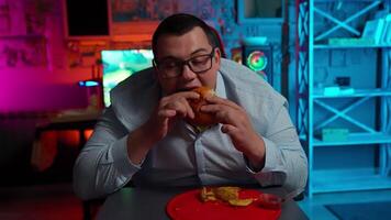 A man eating a hot dog in front of a computer video