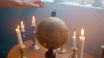 A globe on a table with candles and a hand reaching for it video