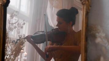 A woman playing the violin in front of a mirror video