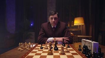 A man in a suit sitting at a table with a chess board video