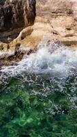 Turquoise sea waves crashing against rugged rocks on a sunny day create a stunning display of white foam, highlighting the vibrant, clear water and showcasing nature's raw energy video