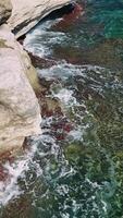 Turquoise waves crashing against rugged cliffs create a serene inlet under the bright summer sun, showcasing the natural beauty of a breathtaking coastline video