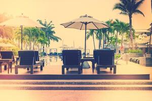 A row of chairs and umbrellas sit near a pool photo